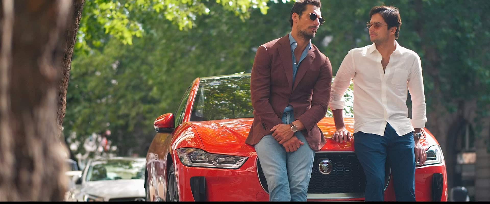 Person in yellow puffer jacket adjusting small sunglasses while standing outdoors against red-trimmed windows with graffiti in sunlight.