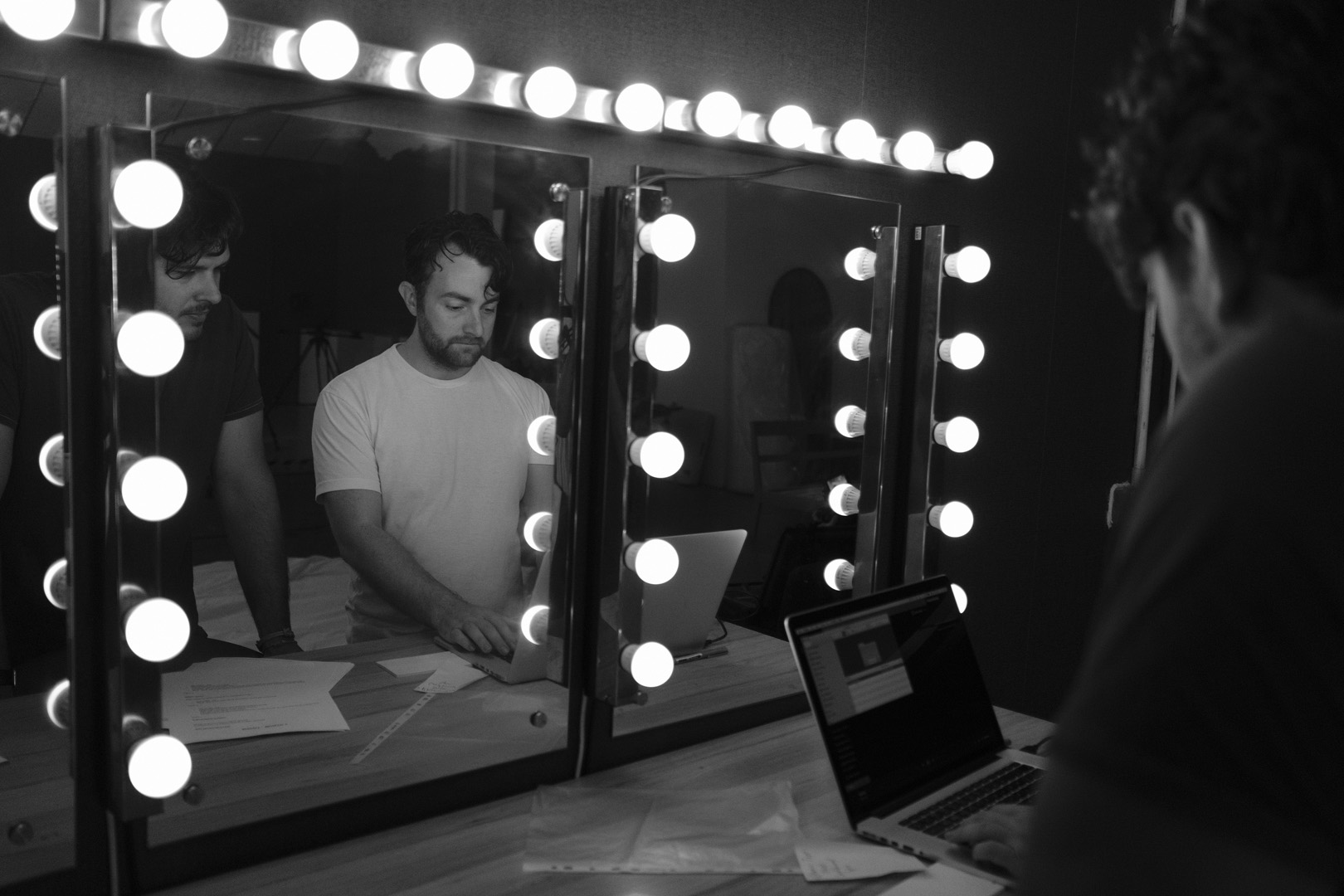 A black and white, close-up shot of a woman covering her face with one hand, palm forward, in a gesture that suggests a refusal to be seen or to face the viewer. She is wearing hoop earrings and dark lipstick.